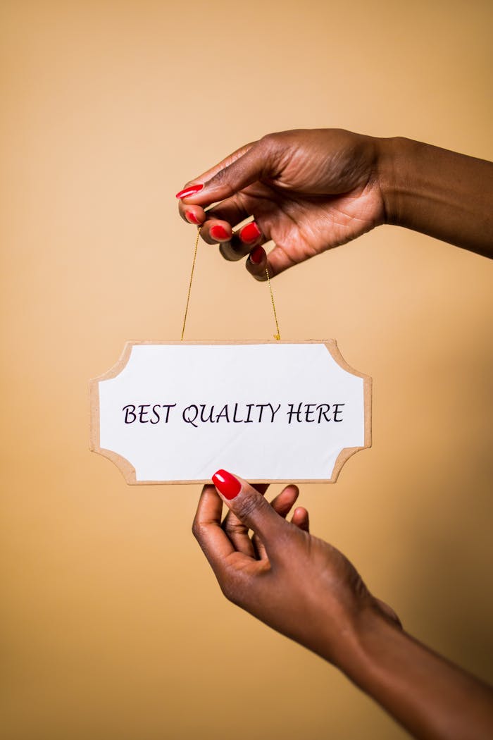Stylish female hands with red nails holding a sign that says 'Best Quality Here' against a soft background.